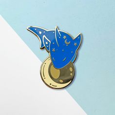 a blue and gold enamel pin with an astronaut's hat on top of the moon