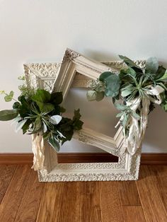 a white frame with flowers and greenery on the floor in front of a wall