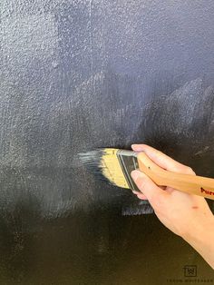 a person holding a paintbrush and painting the wall with black color on it,