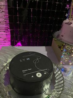 a black cake sitting on top of a glass plate next to a purple and white wall