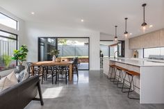 a modern kitchen and dining area in a house with concrete floors, large windows, an open floor plan, and lots of natural greenery