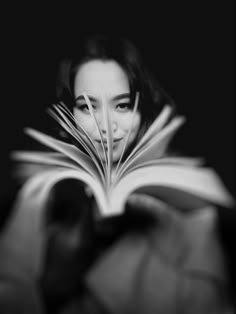 a woman is reading a book with her face hidden by the pages in black and white