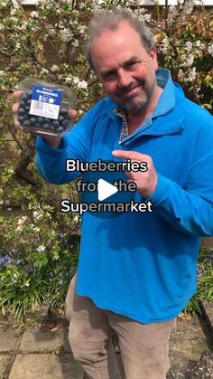 a man in blue shirt holding up a cell phone with the text blueberries from the supermarket