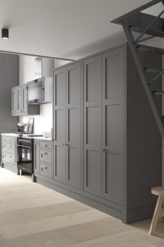 a kitchen with gray cabinets and stairs leading up to the upper floor, next to a stove top oven