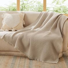 a couch with a blanket on top of it next to two pillows and a window