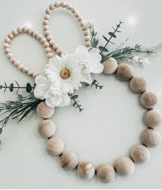 a wooden beaded necklace with flowers and greenery around it on a white surface