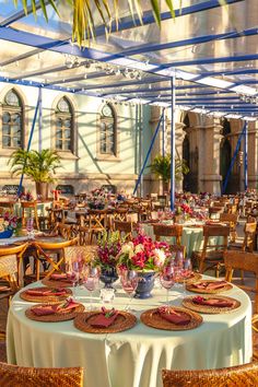 an outdoor dining area with wicker chairs and round tables set for two, surrounded by palm trees