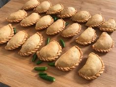 many small pastries are arranged on a wooden cutting board with green peppers next to them