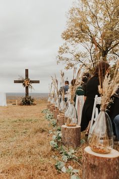 people sitting in front of a cross on top of a grass covered field next to trees