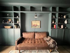 a brown couch sitting on top of a wooden floor next to a bookshelf