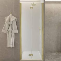 a white and gold shower in a bathroom next to a mirror with towels hanging on it