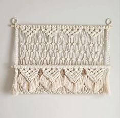 a macrame wall hanging with tassels and beads on the bottom, in white