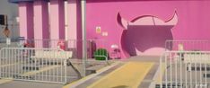 there is a pink building with an animal head painted on it's side and white fence around the entrance