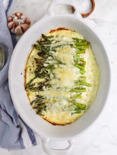 an oval casserole dish with asparagus and cheese in it on a white table