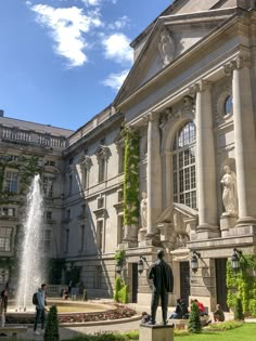 a large building with a fountain in front of it and people sitting on the lawn