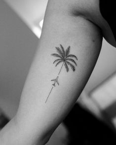 a woman's arm with a palm tree and an arrow tattoo on the left forearm