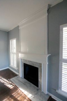 an empty living room with a fireplace in the center and shuttered windows on both sides