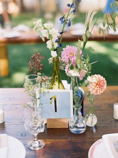 the table is set with vases and flowers on it, along with place cards