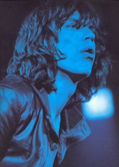 a man with long hair wearing a black leather jacket and blue lighting in the background