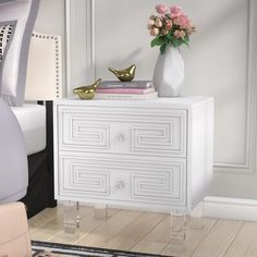 a white dresser with gold accents and flowers on top in a bedroom area next to a bed