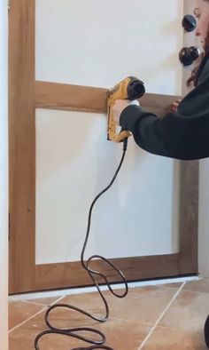 a woman is using an electric nailer on the wall in front of a door