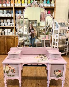 a pink vanity with flowers painted on it and a woman taking a photo in the mirror