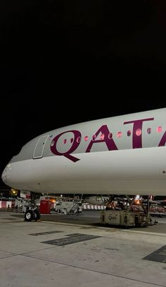 a large jetliner sitting on top of an airport tarmac at night with the word qatar painted on it