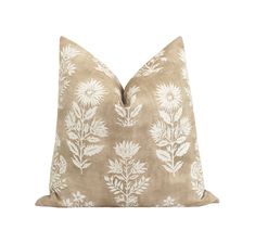 a tan pillow with white flowers on the front and back, against a white background