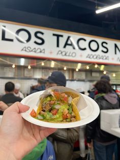 a person holding up a paper plate with food on it at a taco shop