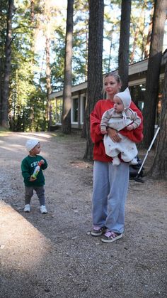 two people standing in the woods with one holding a baby