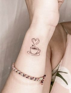 a person with a tattoo on their arm holding a coffee cup in the shape of a heart