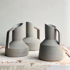 three gray vases sitting on top of a table next to each other in front of a white wall