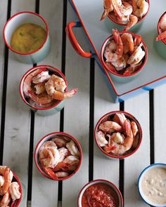 several small bowls filled with shrimp next to dipping sauces