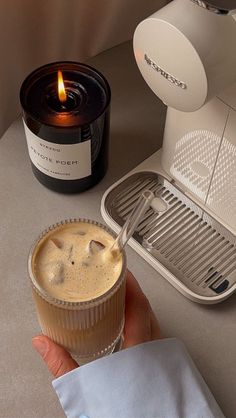 a person is holding a drink in front of a blender and a candle on a table