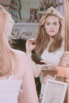 a woman is standing in front of a mirror and looking at her reflection while brushing her hair