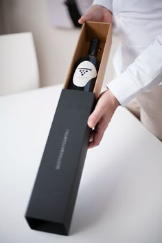 a person holding a wine bottle in a black box on a white table with other people