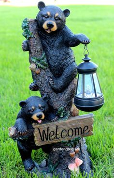 two black bears sitting on top of a tree next to a welcome sign