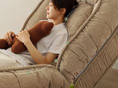 a woman sitting in a chair with a teddy bear on her lap and holding the pillow