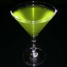 a green drink sitting in a glass on top of a black table with light coming from behind it