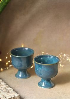 two blue cups sitting next to each other on top of a table with lights in the background