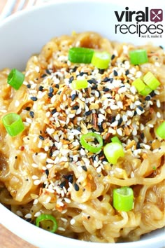 a white bowl filled with noodles covered in sesame seeds and chopped green onions next to a fork