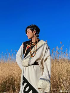 a woman dressed in native american clothing standing in a field with tall grass and blue sky behind her