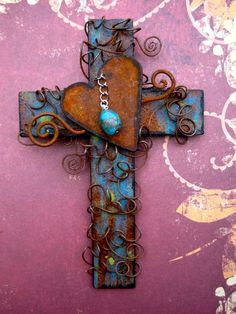 a metal cross with a heart hanging from it's side on a pink wall