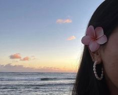 a woman standing on top of a beach next to the ocean with a flower in her hair