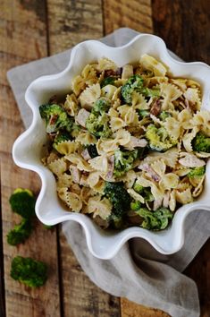 a white bowl filled with pasta and broccoli on top of a wooden table