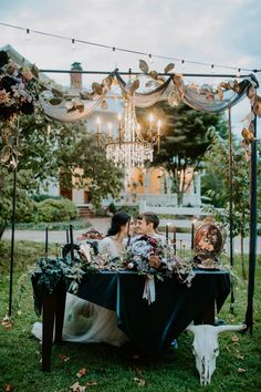 a bride and groom sitting at a table under a chandelier with flowers on it