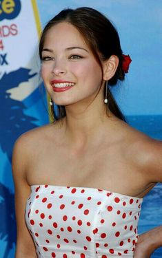 a woman in a white and red polka dot dress smiles at the camera with her hand on her hip