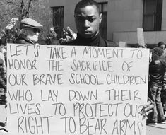 a man holding a sign that reads let's take a moment to honk the sacrifice of our brave school children who lay down their lives to protect our right to bear arms