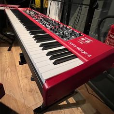 a red and white keyboard sitting on top of a hard wood floor next to a wall