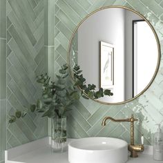 a white sink sitting under a round mirror next to a vase filled with green plants